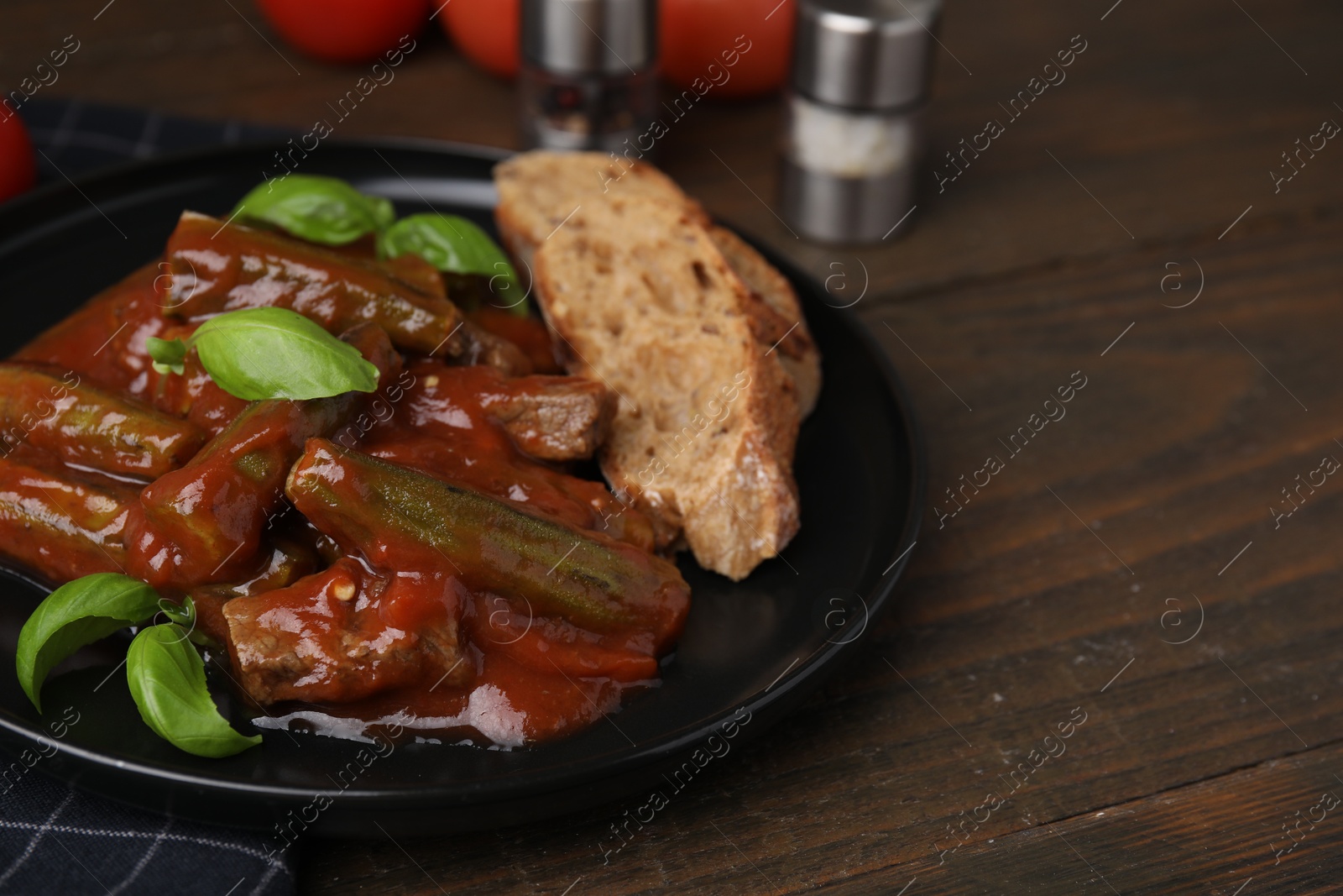 Photo of Tasty stew with okra, tomato sauce, bread and basil on wooden table, closeup. Space for text