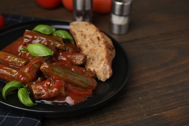 Photo of Tasty stew with okra, tomato sauce, bread and basil on wooden table, closeup. Space for text