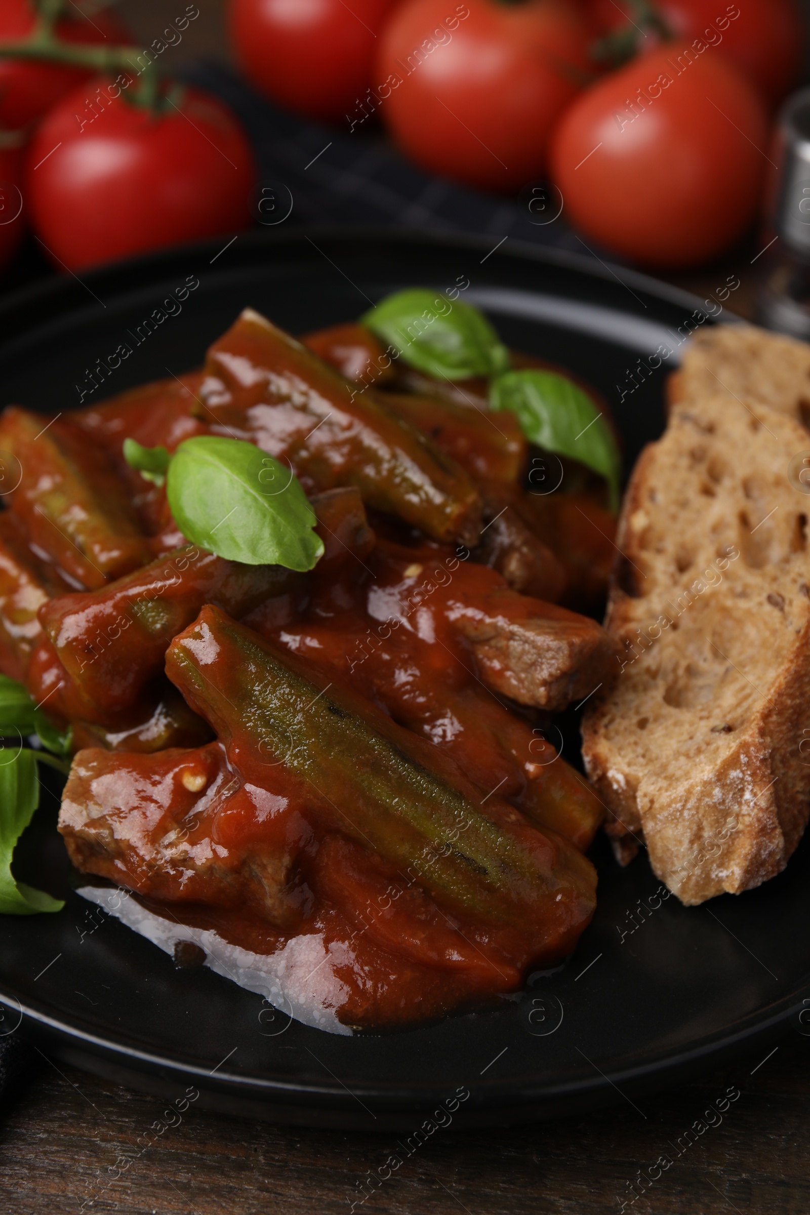 Photo of Tasty stew with okra, tomato sauce, bread and basil on wooden table, closeup