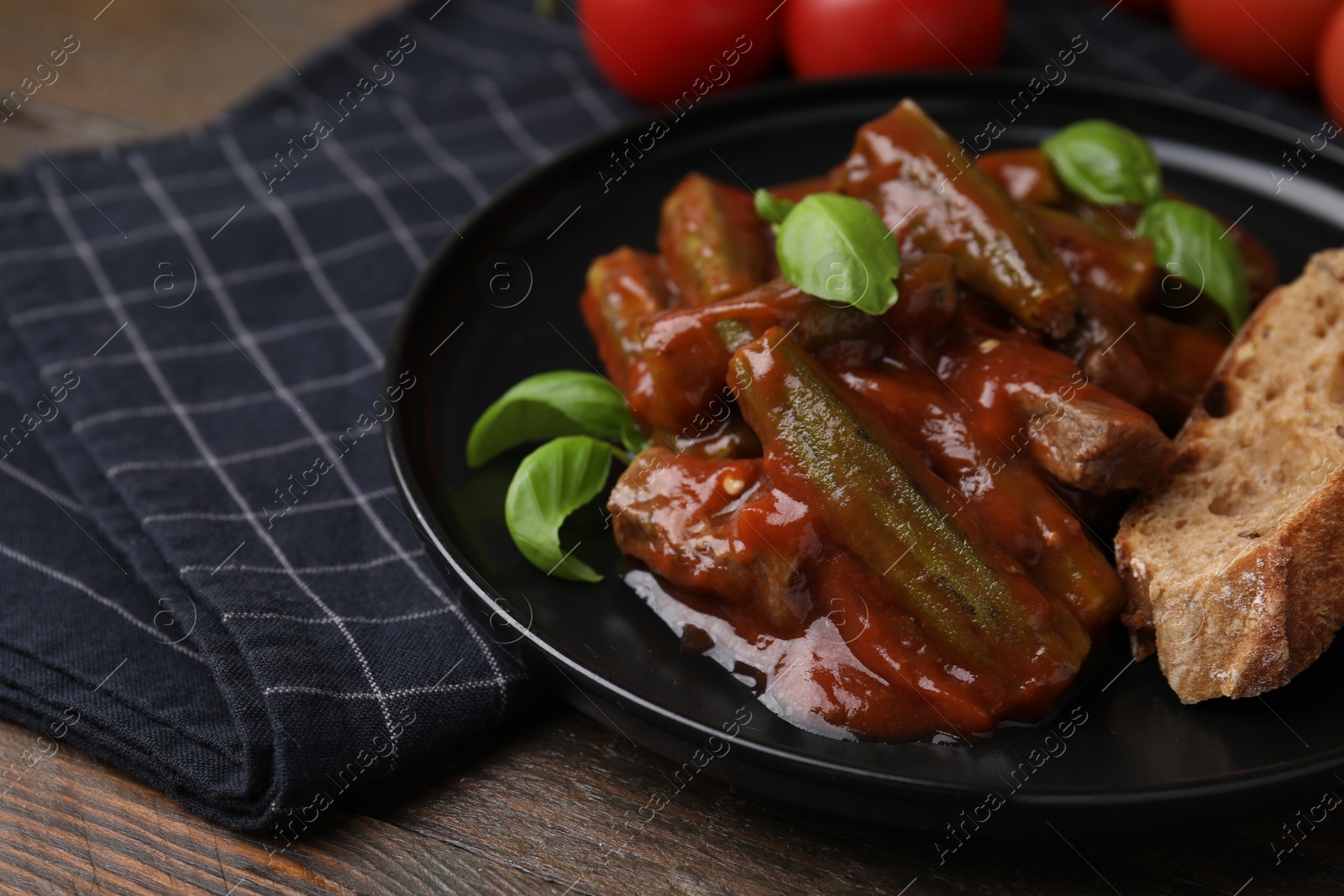 Photo of Tasty stew with okra, tomato sauce, bread and basil on wooden table, closeup