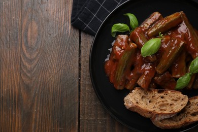 Photo of Tasty stew with okra, tomato sauce, bread and basil on wooden table, top view. Space for text