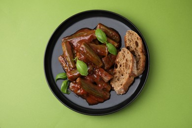 Photo of Tasty stew with okra, tomato sauce, bread and basil on light green background, top view