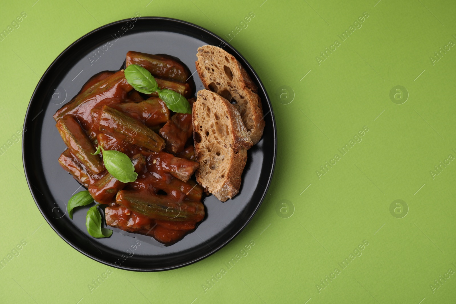 Photo of Tasty stew with okra, tomato sauce, bread and basil on light green background, top view. Space for text