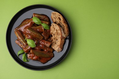 Photo of Tasty stew with okra, tomato sauce, bread and basil on light green background, top view. Space for text