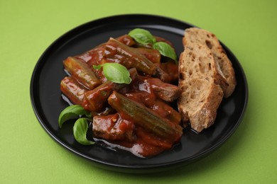 Photo of Tasty stew with okra, tomato sauce, bread and basil on light green background, closeup