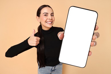 Image of Happy woman showing mobile phone with blank screen on dark beige background. Mockup for design