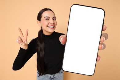 Image of Happy woman showing mobile phone with blank screen on dark beige background. Mockup for design