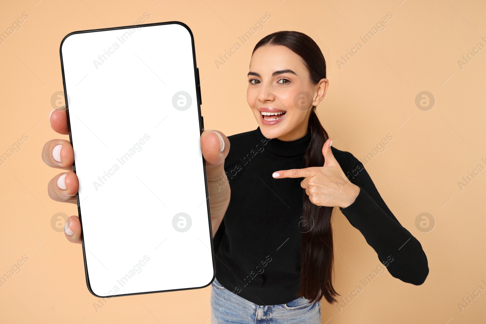 Image of Happy woman pointing at mobile phone with blank screen on dark beige background. Mockup for design