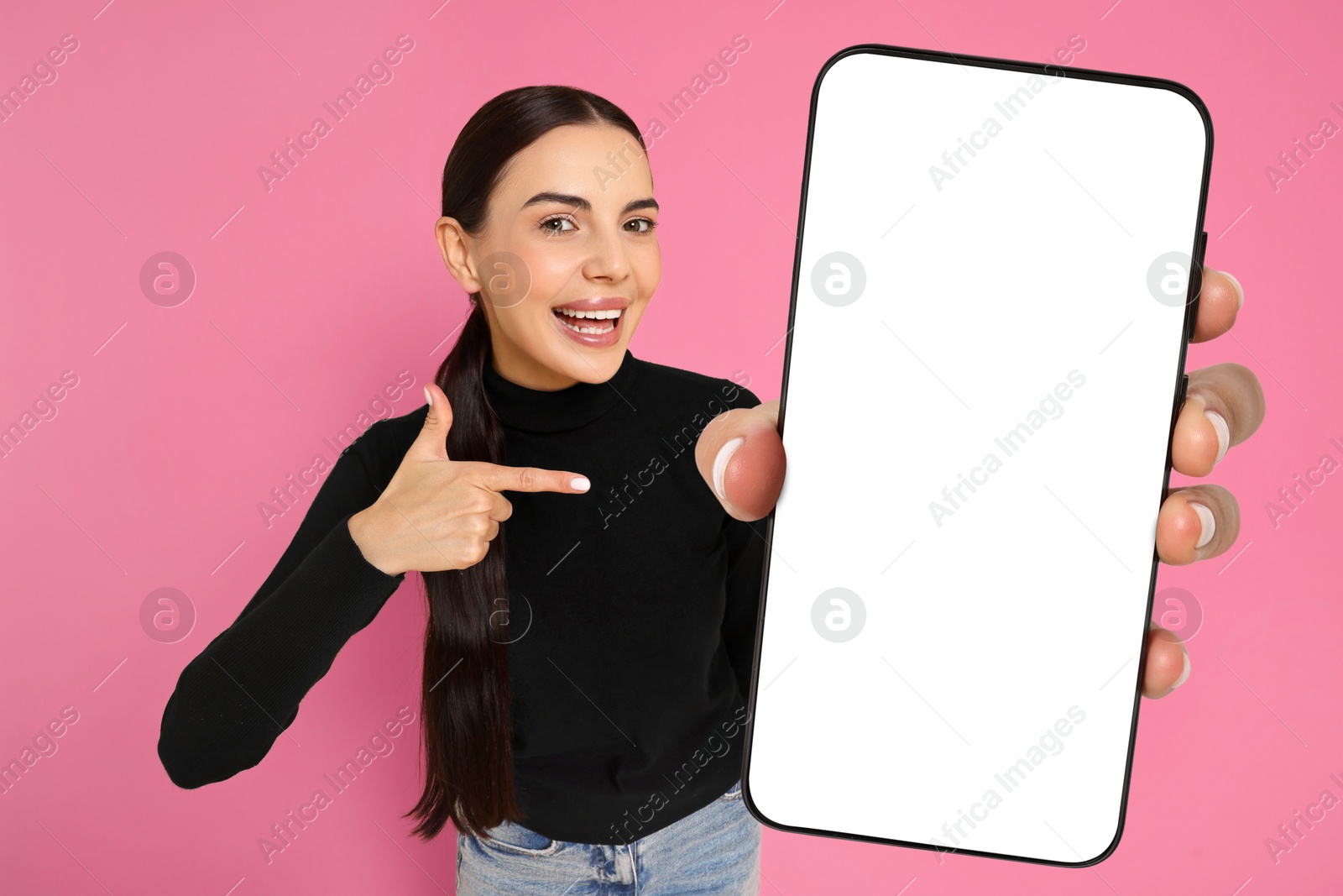 Image of Happy woman pointing at mobile phone with blank screen on pink background. Mockup for design