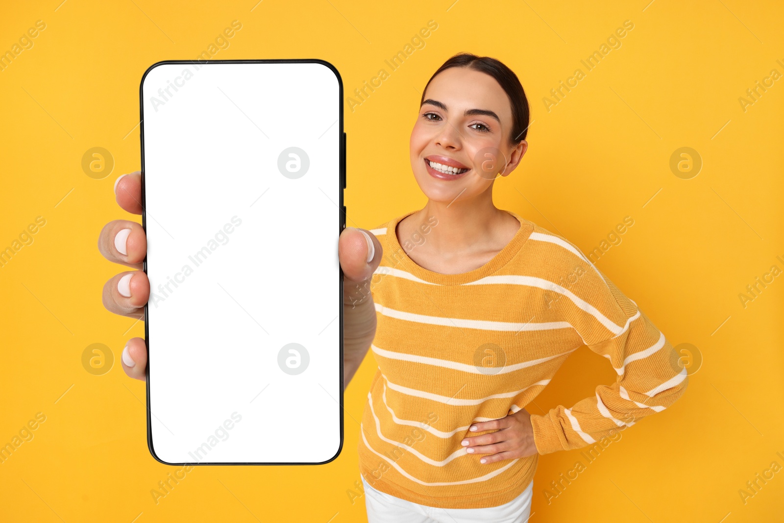 Image of Happy woman showing mobile phone with blank screen on orange background. Mockup for design