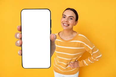 Image of Happy woman showing mobile phone with blank screen on orange background. Mockup for design