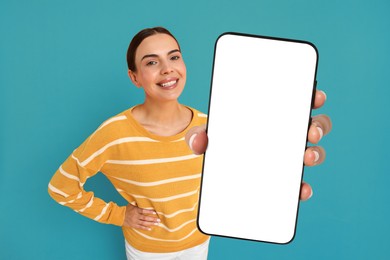 Happy woman showing mobile phone with blank screen on light blue background. Mockup for design