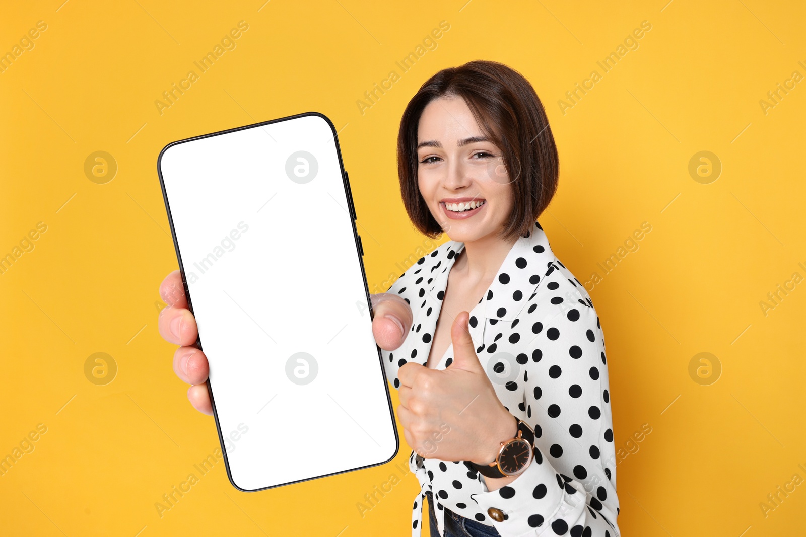 Image of Happy woman showing mobile phone with blank screen on orange background. Mockup for design