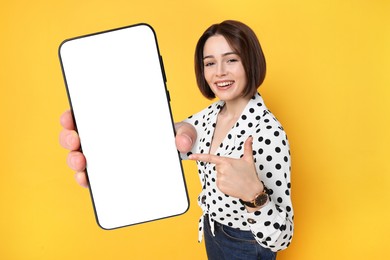 Happy woman pointing at mobile phone with blank screen on golden background. Mockup for design