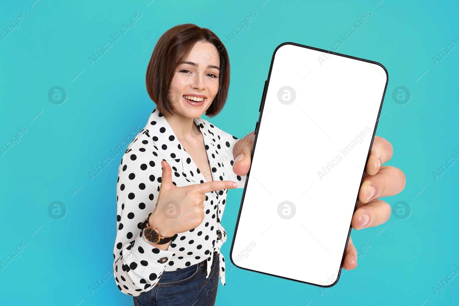 Image of Happy woman pointing at mobile phone with blank screen on light blue background. Mockup for design