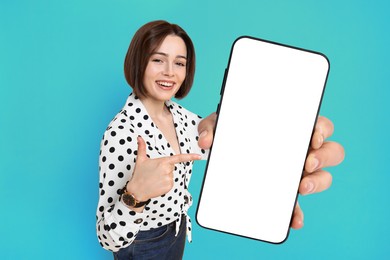 Happy woman pointing at mobile phone with blank screen on light blue background. Mockup for design