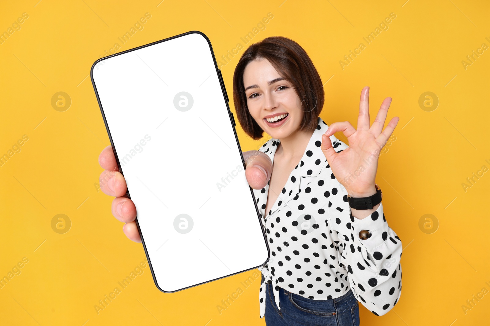 Image of Happy woman showing mobile phone with blank screen on orange background. Mockup for design