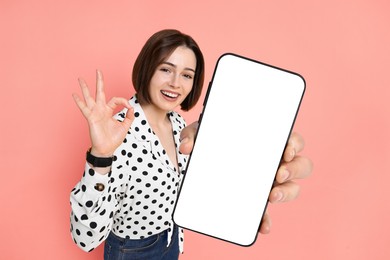 Image of Happy woman showing mobile phone with blank screen on beige pink background. Mockup for design