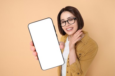 Happy woman showing mobile phone with blank screen on dark beige background. Mockup for design