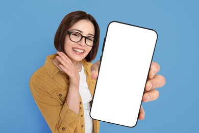 Happy woman showing mobile phone with blank screen on blue background. Mockup for design