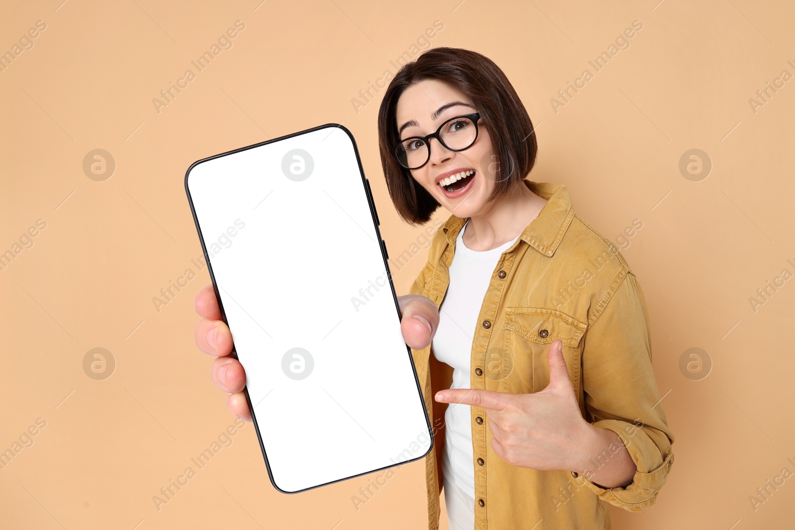 Image of Happy woman pointing at mobile phone with blank screen on dark beige background. Mockup for design