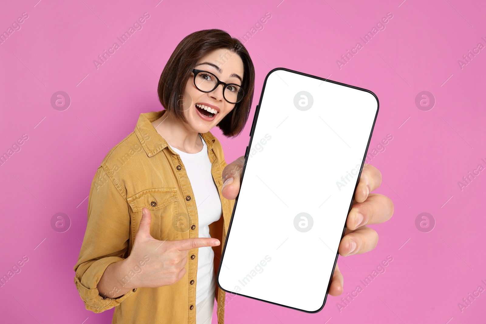 Image of Happy woman pointing at mobile phone with blank screen on magenta background. Mockup for design