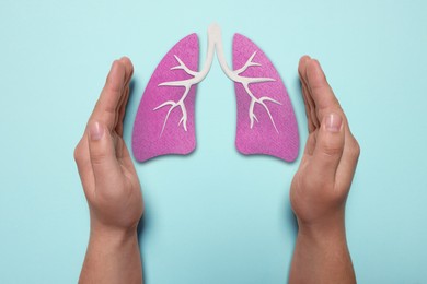 Image of Woman holding hands near illustration of lungs on light blue background, closeup. Asthma and other respiratory diseases