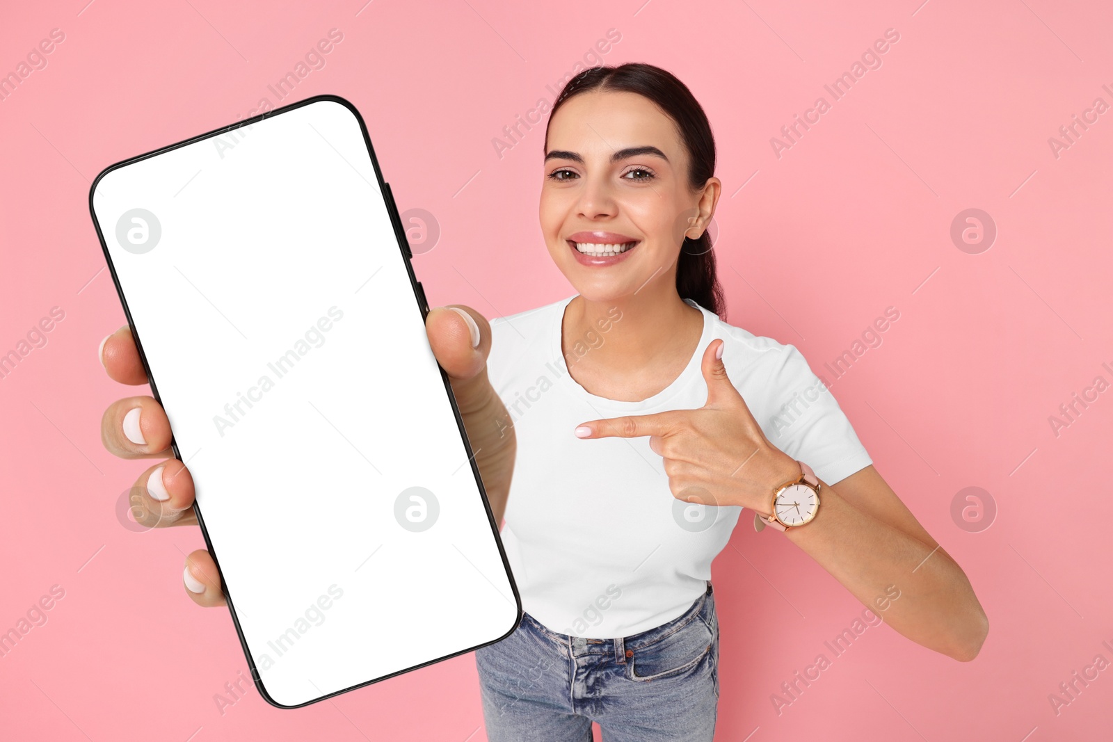 Image of Happy woman pointing at mobile phone with blank screen on pink background. Mockup for design