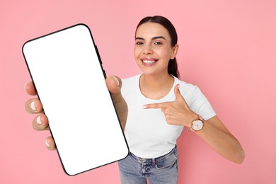 Happy woman pointing at mobile phone with blank screen on pink background. Mockup for design