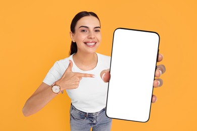 Happy woman pointing at mobile phone with blank screen on orange background. Mockup for design