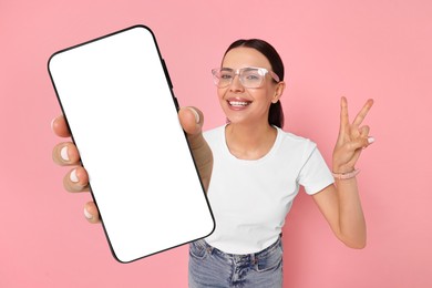 Image of Happy woman showing mobile phone with blank screen on pink background. Mockup for design