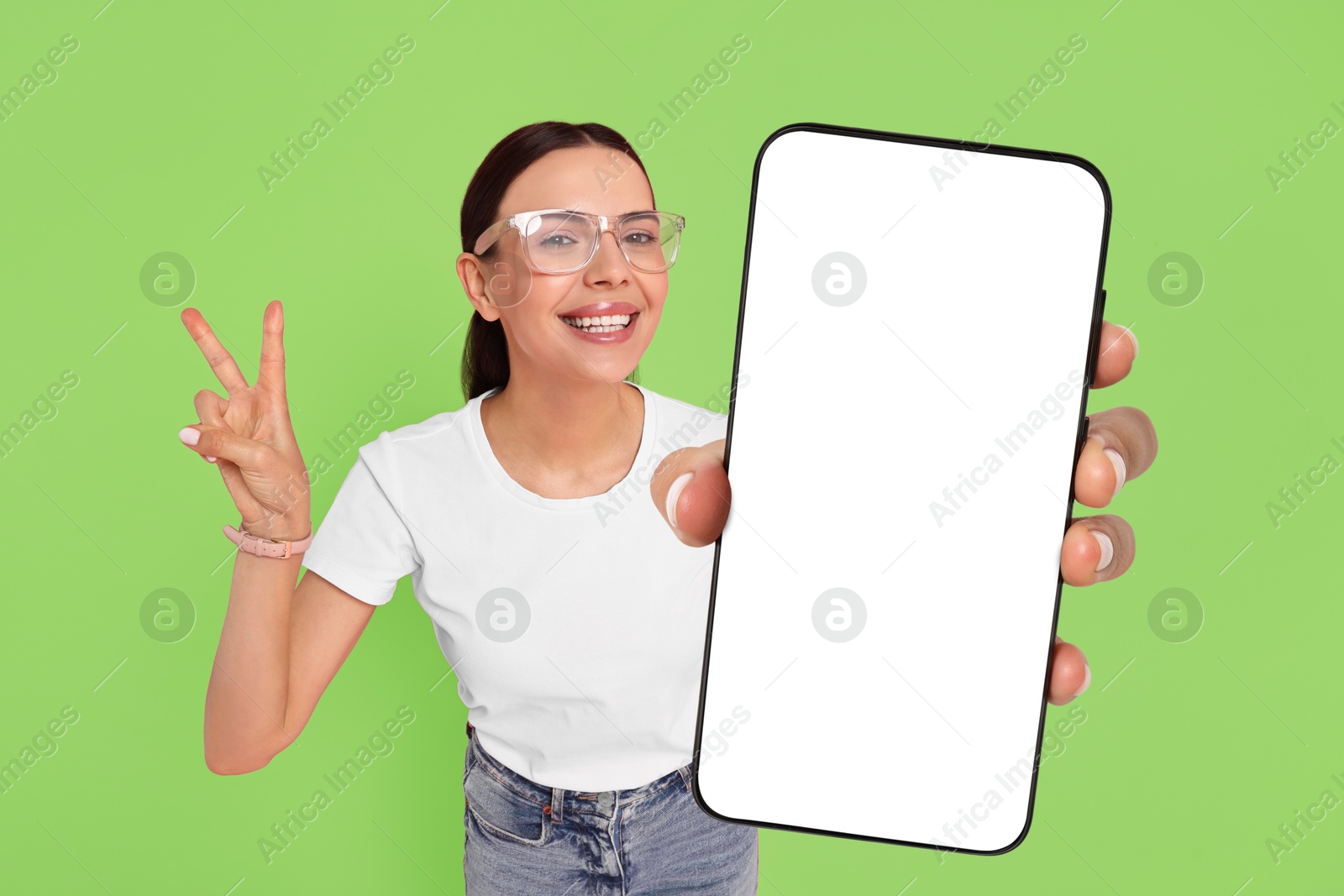 Image of Happy woman showing mobile phone with blank screen on green background. Mockup for design