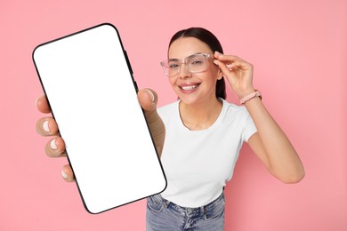 Happy woman showing mobile phone with blank screen on pink background. Mockup for design