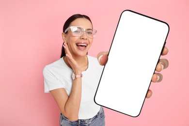 Happy woman showing mobile phone with blank screen on pink background. Mockup for design