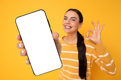 Happy woman showing mobile phone with blank screen on orange background. Mockup for design