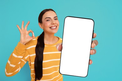 Happy woman showing mobile phone with blank screen on light blue background. Mockup for design