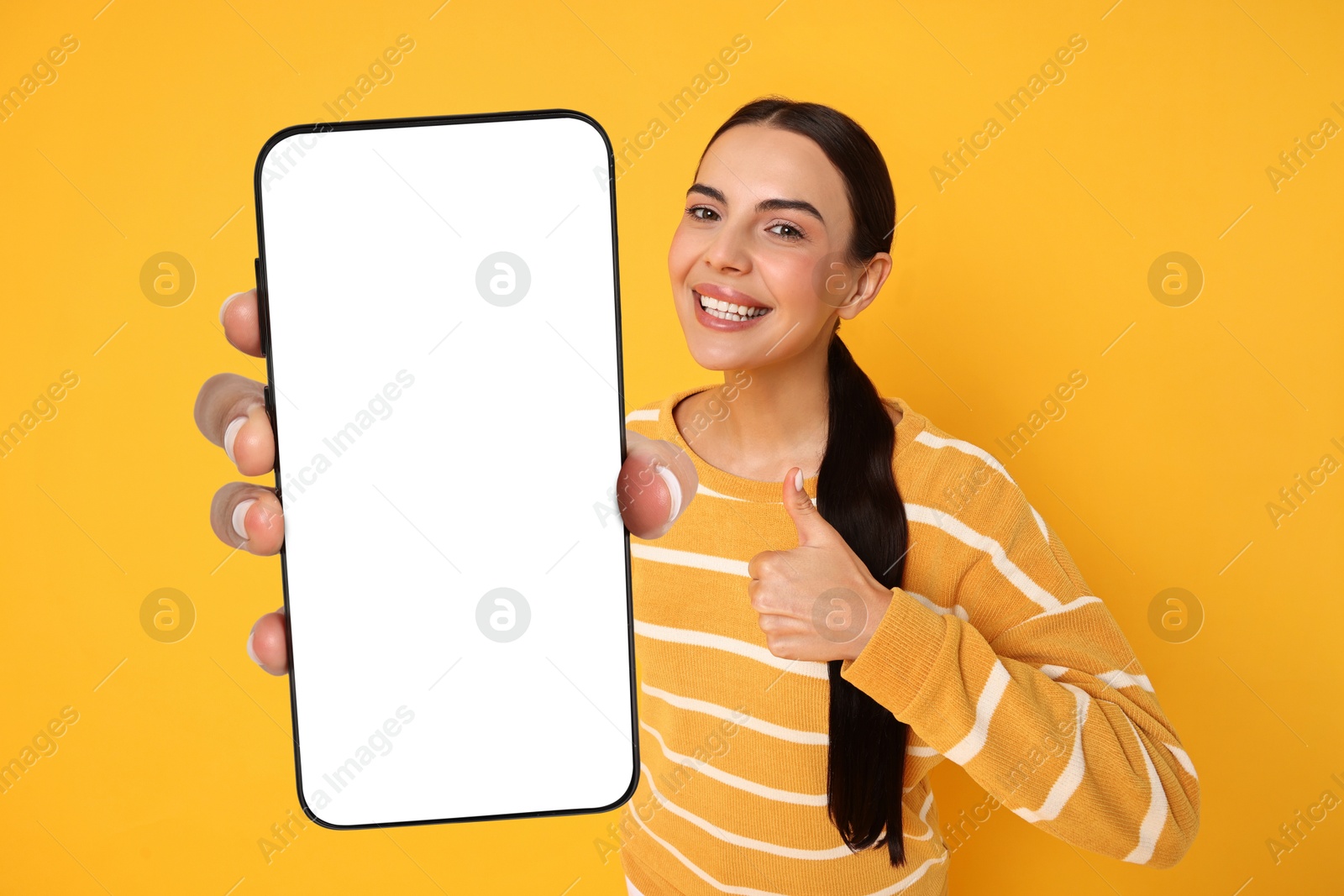 Image of Happy woman showing mobile phone with blank screen on orange background. Mockup for design