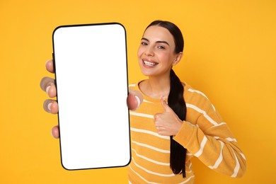 Image of Happy woman showing mobile phone with blank screen on orange background. Mockup for design