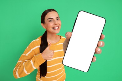 Image of Happy woman showing mobile phone with blank screen on green background. Mockup for design