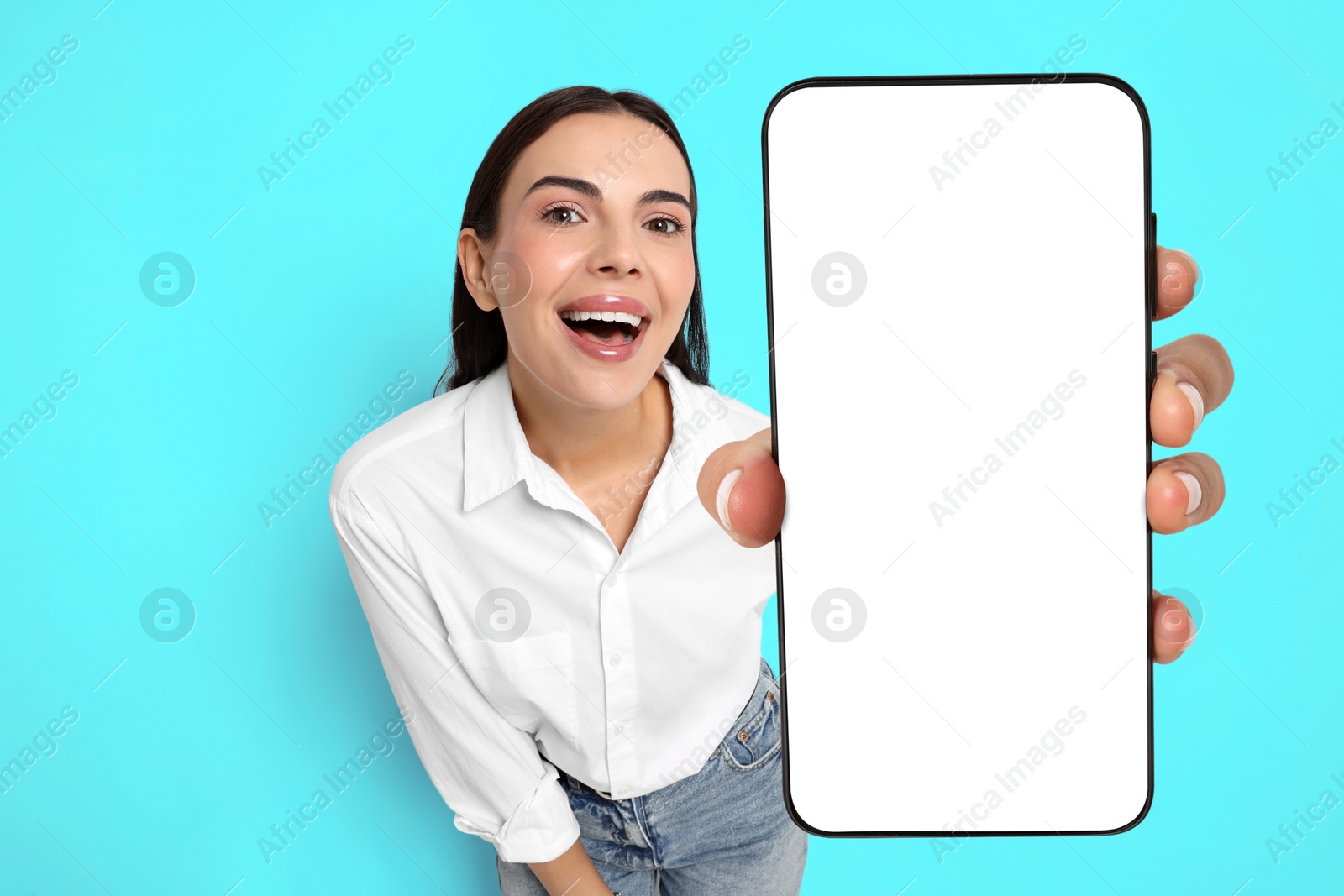 Image of Happy woman showing mobile phone with blank screen on light blue background. Mockup for design