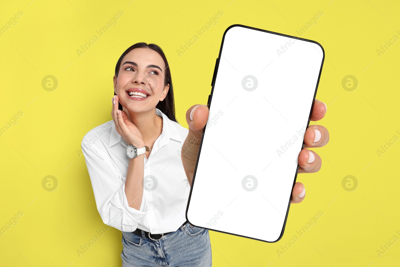 Image of Happy woman showing mobile phone with blank screen on yellow background. Mockup for design