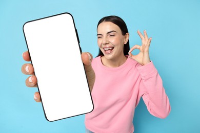 Image of Happy woman showing mobile phone with blank screen on light blue background. Mockup for design