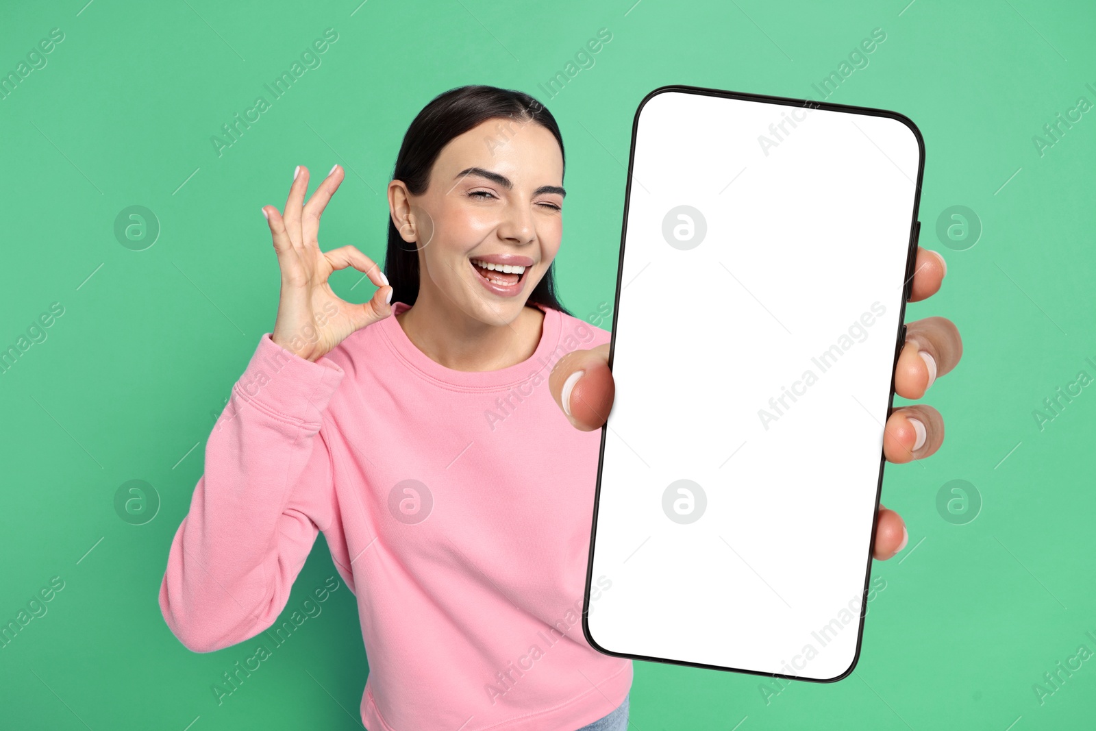 Image of Happy woman showing mobile phone with blank screen on aquamarine background. Mockup for design