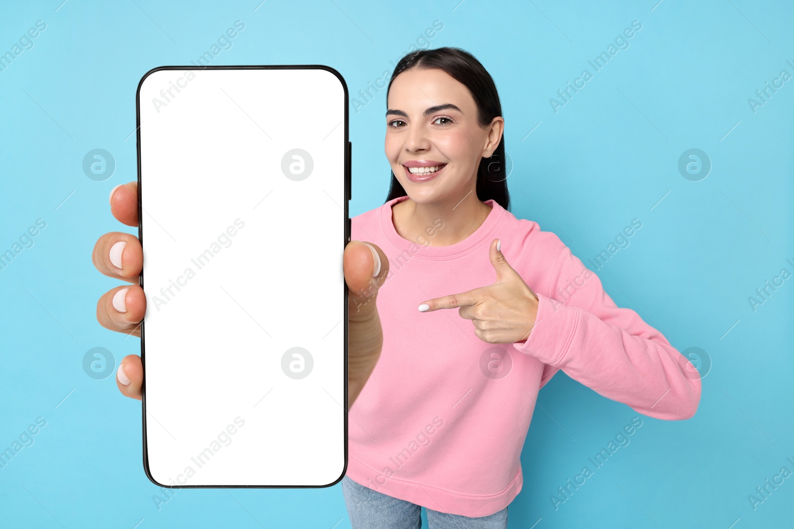 Image of Happy woman pointing at mobile phone with blank screen on light blue background. Mockup for design