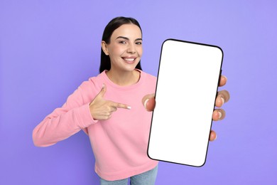 Image of Happy woman pointing at mobile phone with blank screen on blue violet background. Mockup for design