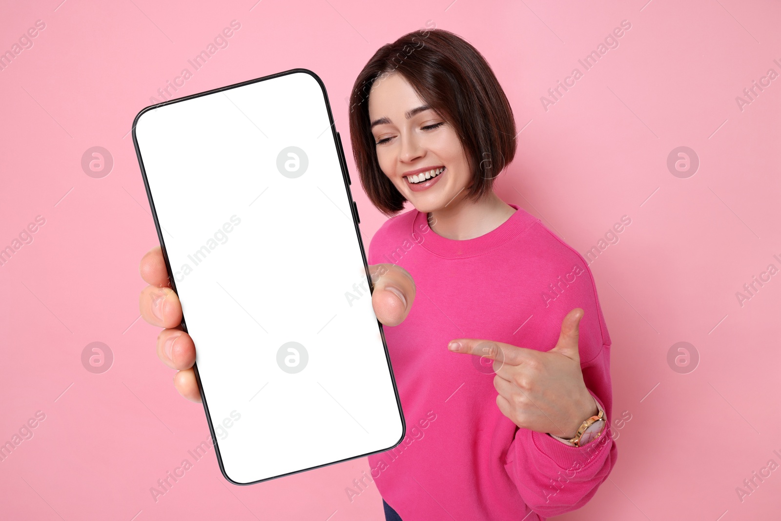 Image of Happy woman pointing at mobile phone with blank screen on pink background. Mockup for design