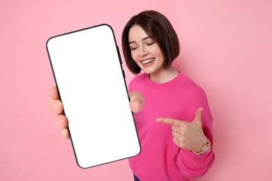 Happy woman pointing at mobile phone with blank screen on pink background. Mockup for design