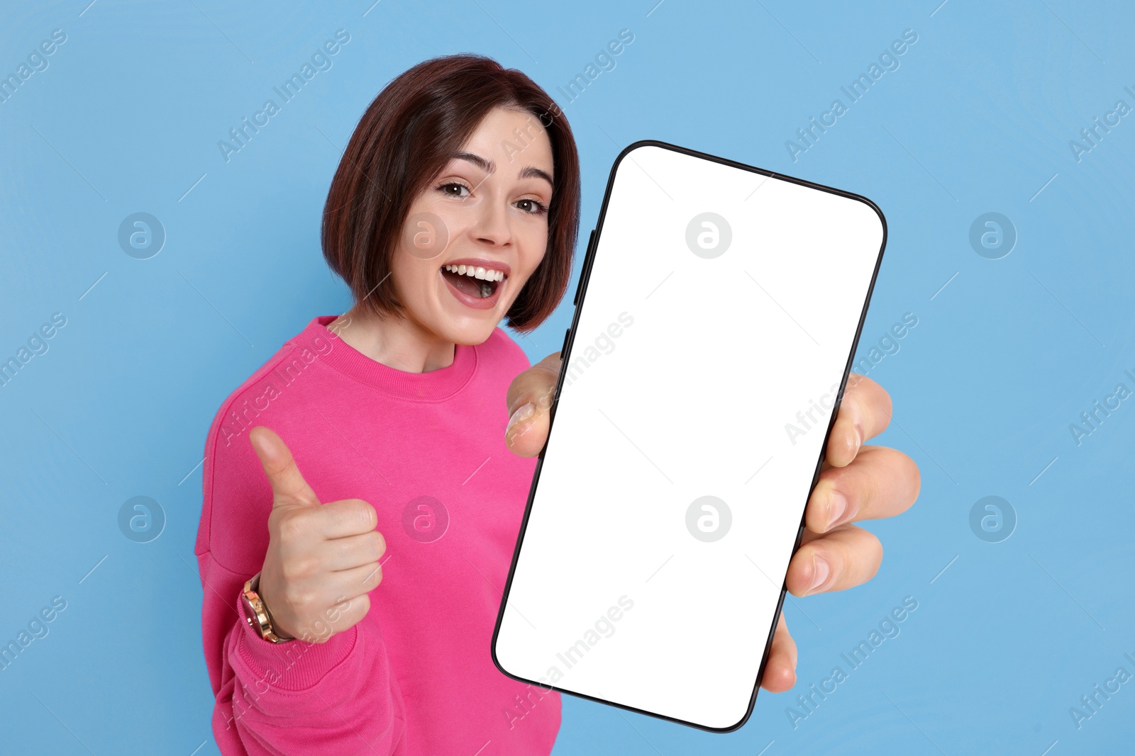 Image of Happy woman showing mobile phone with blank screen on light blue background. Mockup for design