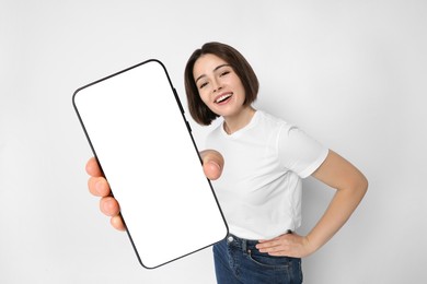 Happy woman showing mobile phone with blank screen on white background. Mockup for design