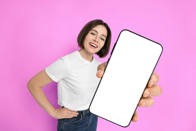 Image of Happy woman showing mobile phone with blank screen on magenta background. Mockup for design